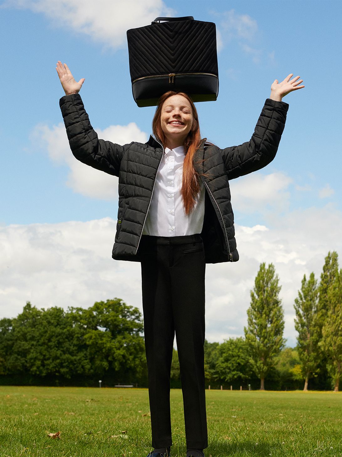 Girl balancing her black school bag on her head.
